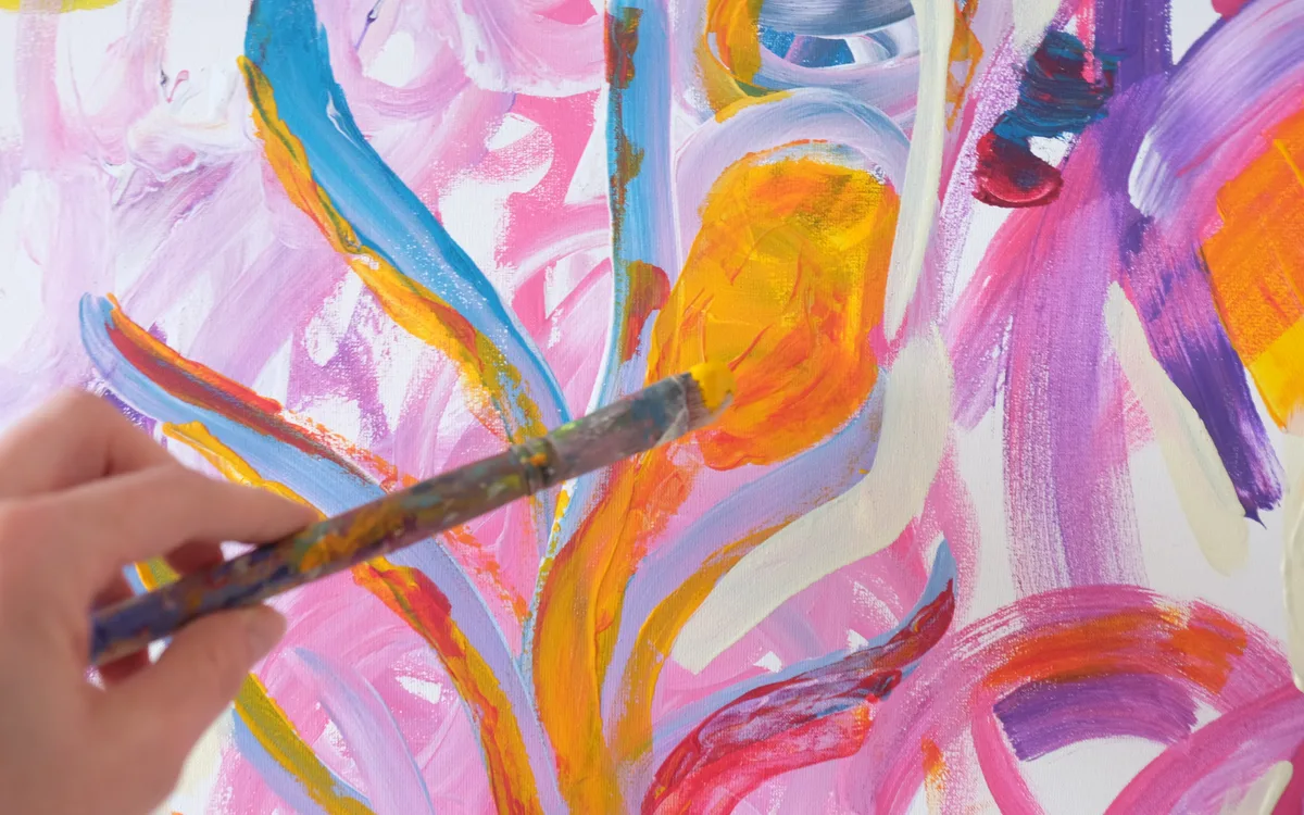Therapeutisches Malen in der Kunsttherapie: Hand führt Pinsel über ein farbenfrohes Bild